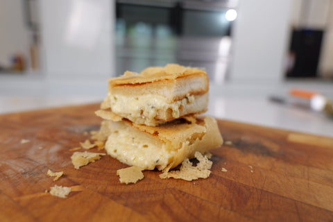 A cheese toasty with a parmesan crumb and melted cheese oozing out of the bread it is sandwiched between